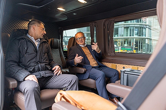 Eine Frau sitzt in einer Flughafen-Limousine und ein Chauffeur hält ihr die Tür auf.
