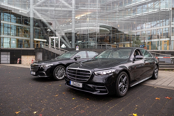 A chauffeur with an umbrella helps a passenger getting in a limousine.